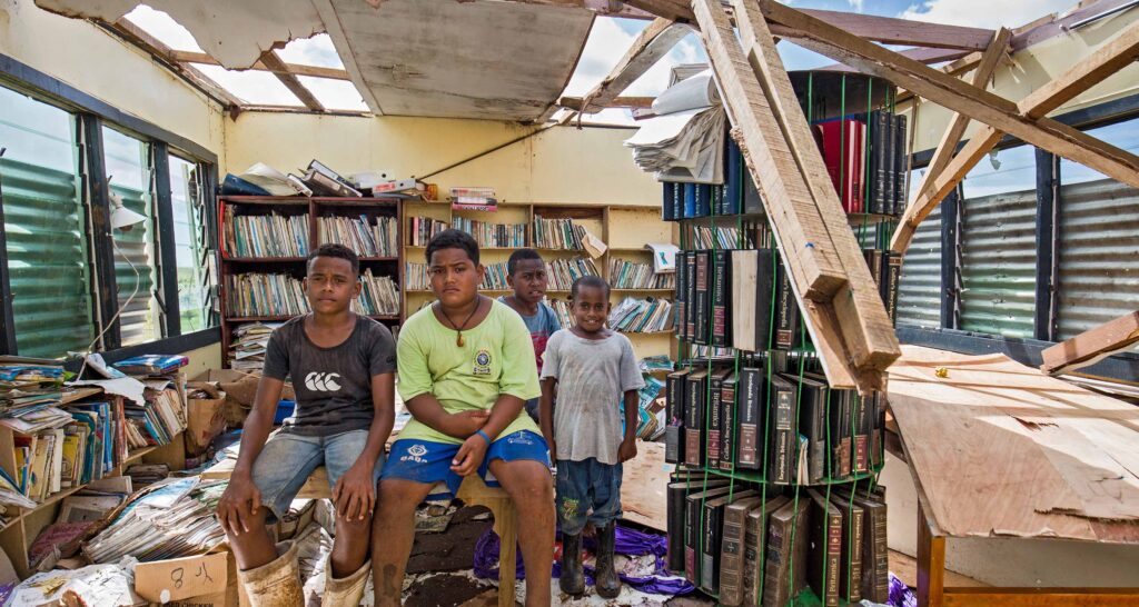 Fijian children sitting in the wreckage of their classroom after it was destroyed by Tropical Cyclone Yasa.